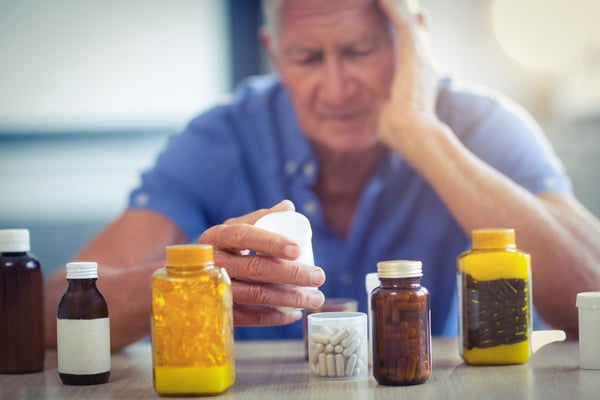 Äldre man med många pillerburkar framför sig ser bekymrad ut