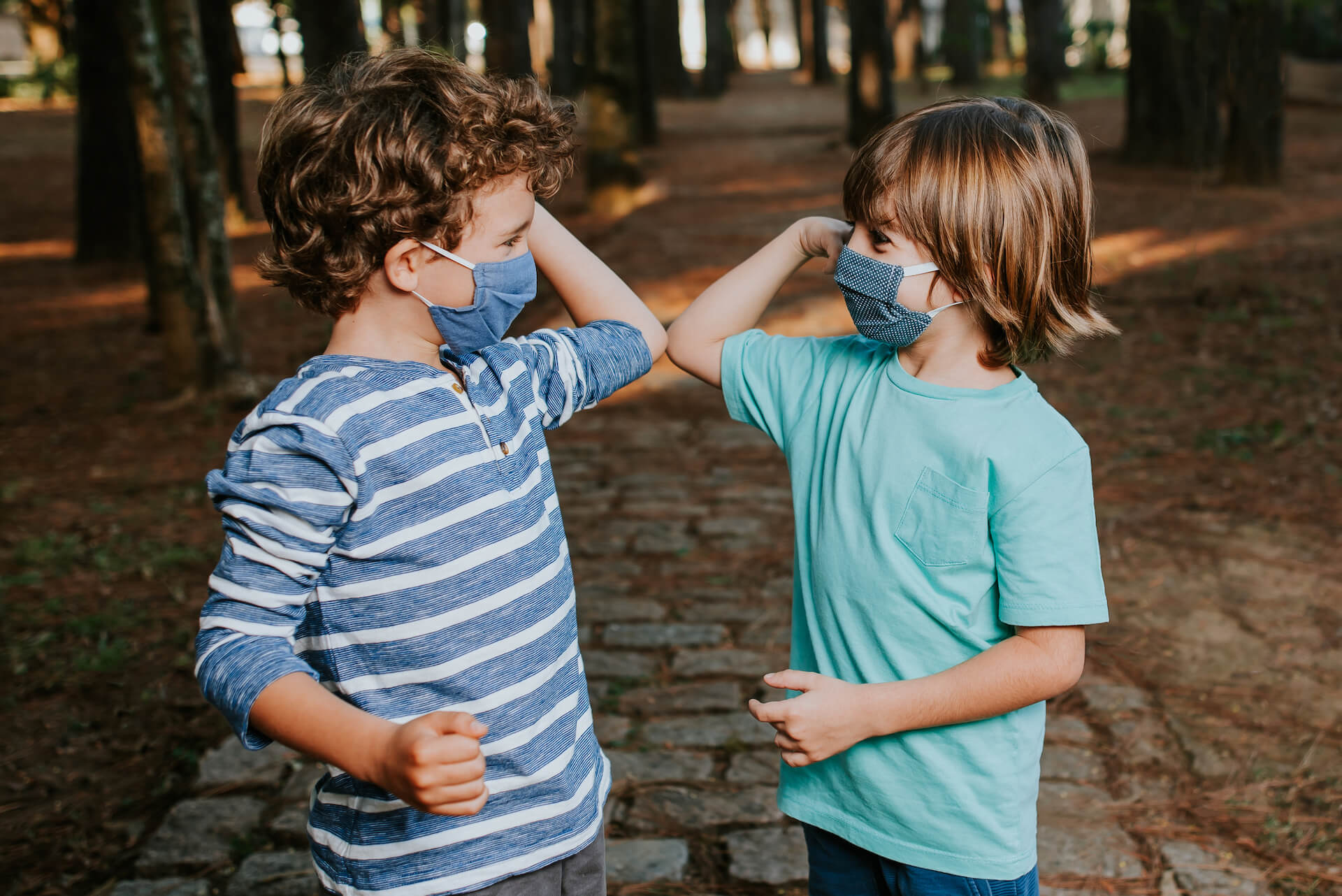 Two young boys greeting each other wearing face mask