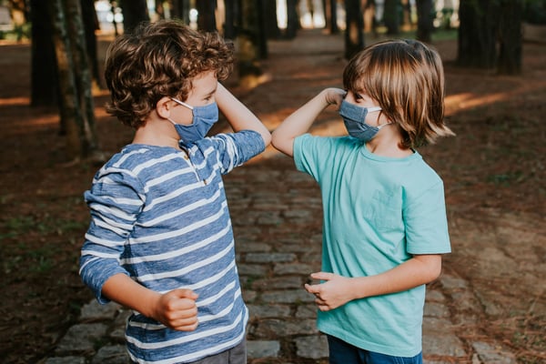 Two young boys wearing face masks greeting with elbows