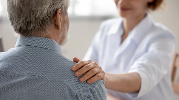 Close up young woman doctor touching senior patient shoulder at meeting in hospital